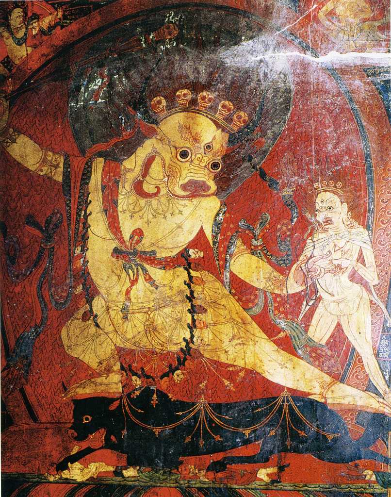 Tibet Guge 08 Tsaparang 05 Yamantaka Temple Yama To the right of the door is a painting of Yama (Tib. Shinje) riding a blue water buffalo. Yama is nude, has a buffalo head, wears a garland of human skulls, has an ornament shaped like a wheel on his breast, his right hand holds a sword topped with a skull, and his left hand holds a loop of rope. On the right is the fierce Dakini Simhaumukha. Snarling and roaring with a gaping large mouth on a white lion face, she stands fierce and menacing with two hands, with protruding fangs, curled tongue, two large round eyes and dark flowing hair. Her left hand clutches to the heart a white skullcup filled with blood. Photo - Th�ni: Westtibet.